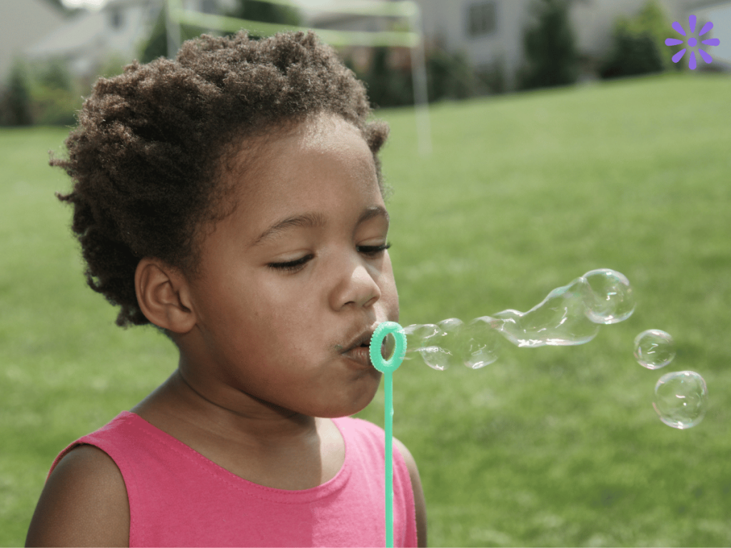 Toddler blowing bubbles at an outside birthday party