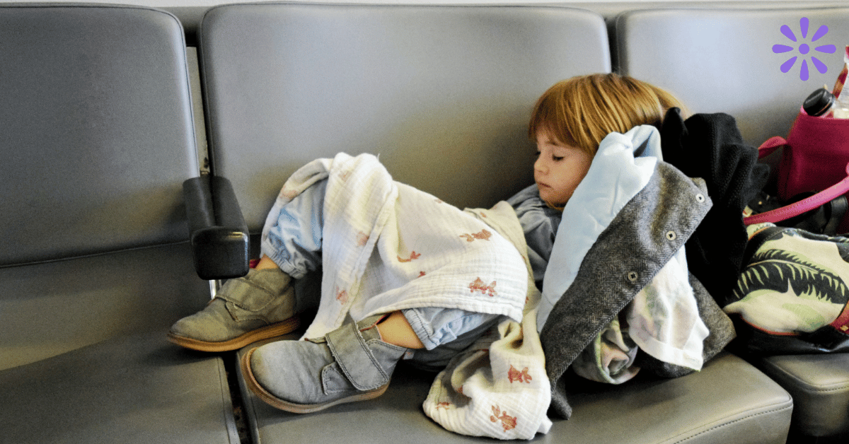 toddler with jet lag sleeping on a row of chairs in an airport